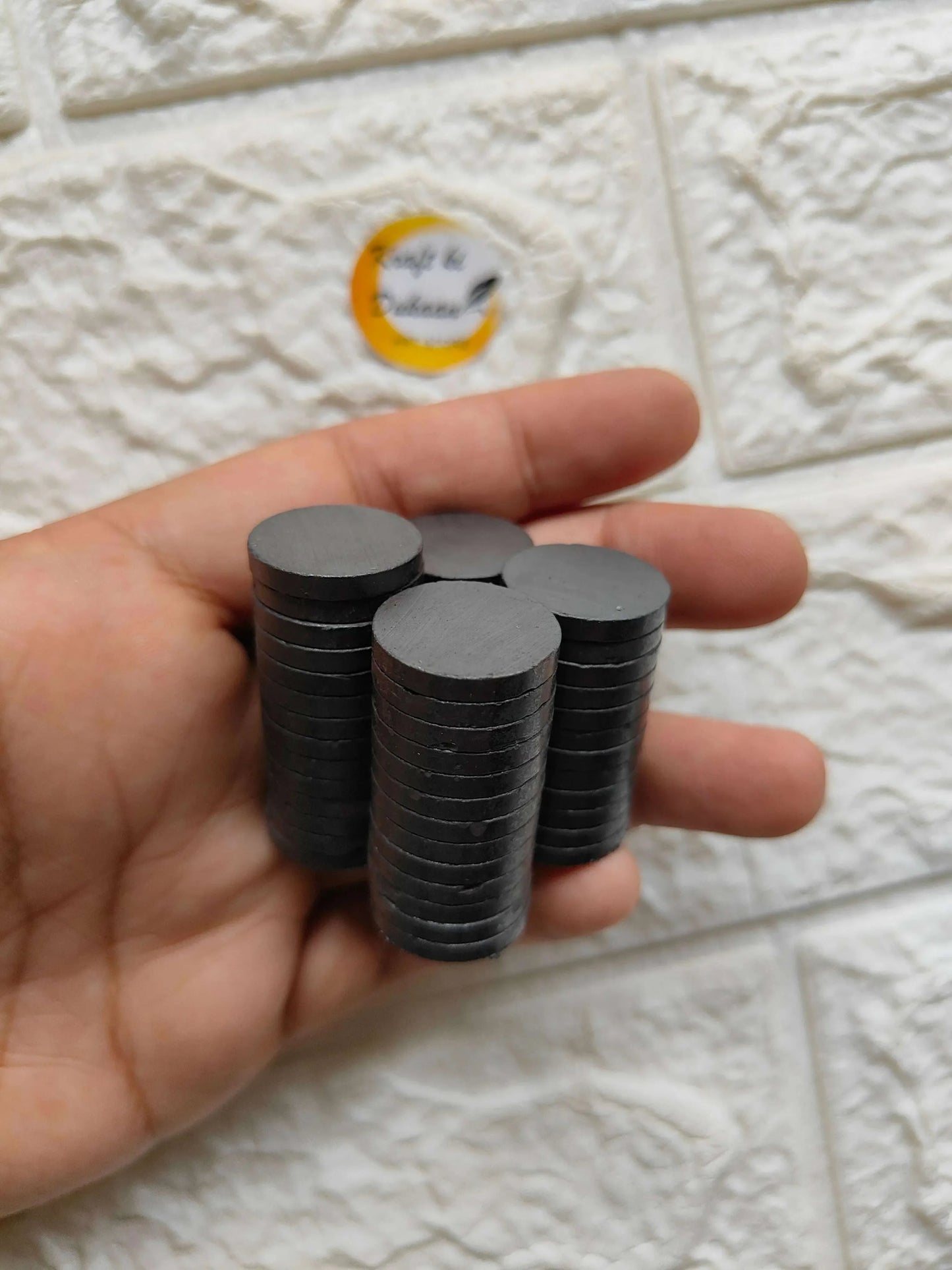 Hand holding stacks of black round magnets, flat circular discs