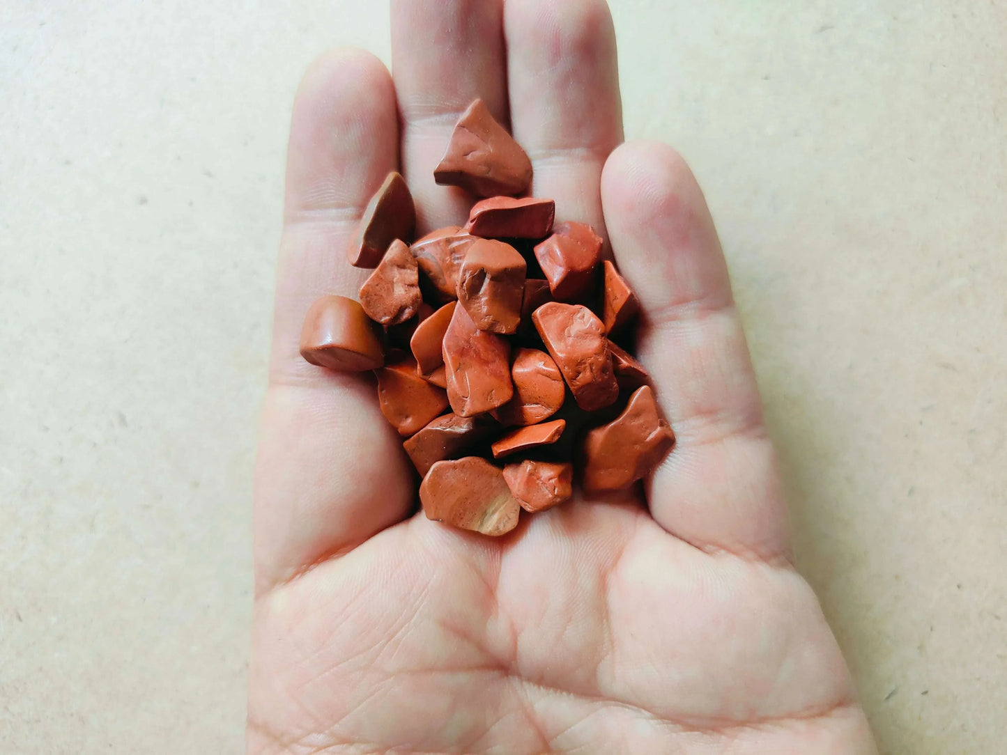 Natural Red Jasper stones in palm: darker reddish-orange jagged pieces