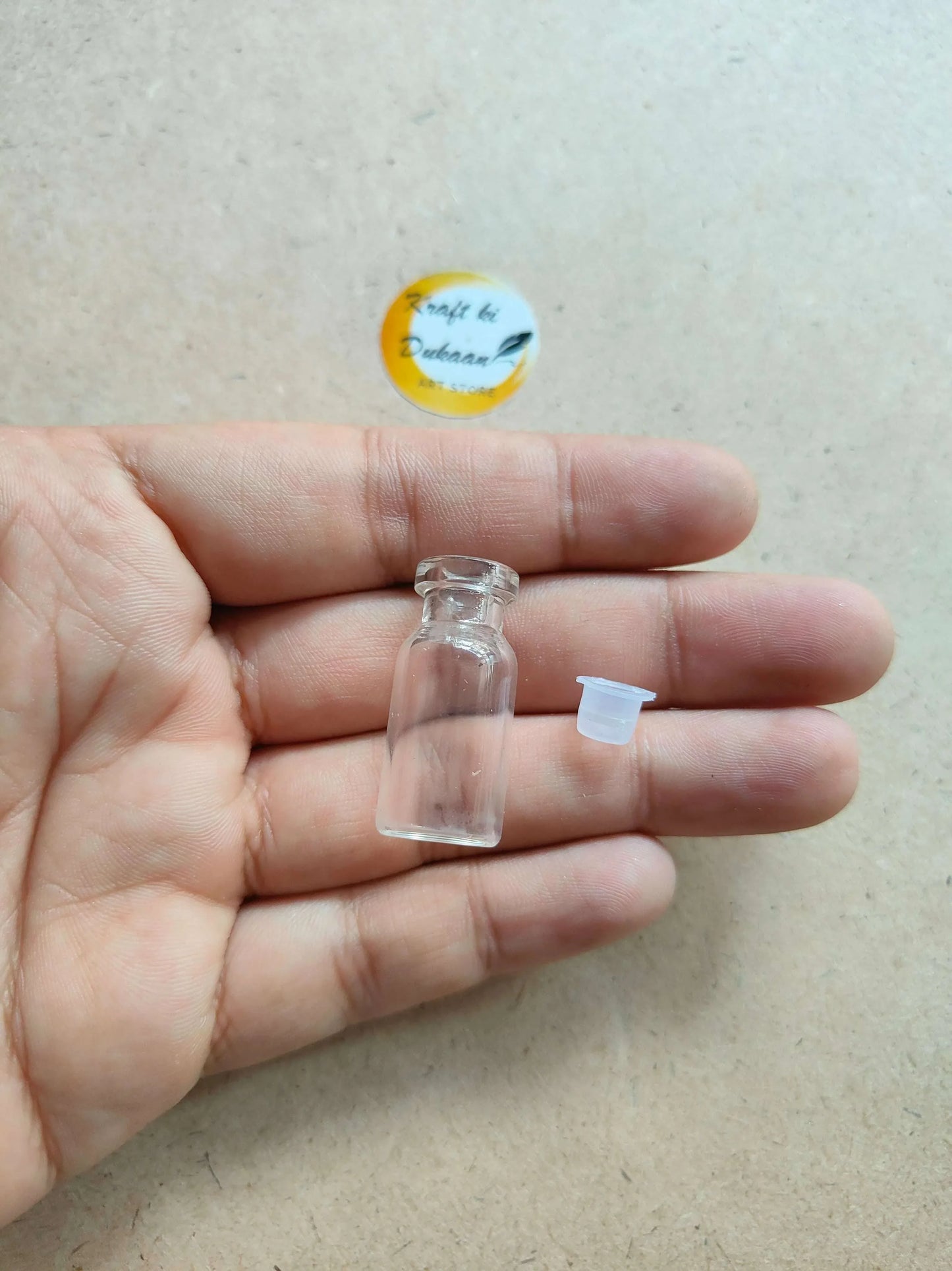 Small clear glass bottle with rubber lid in hand; mini size (pack of 12)