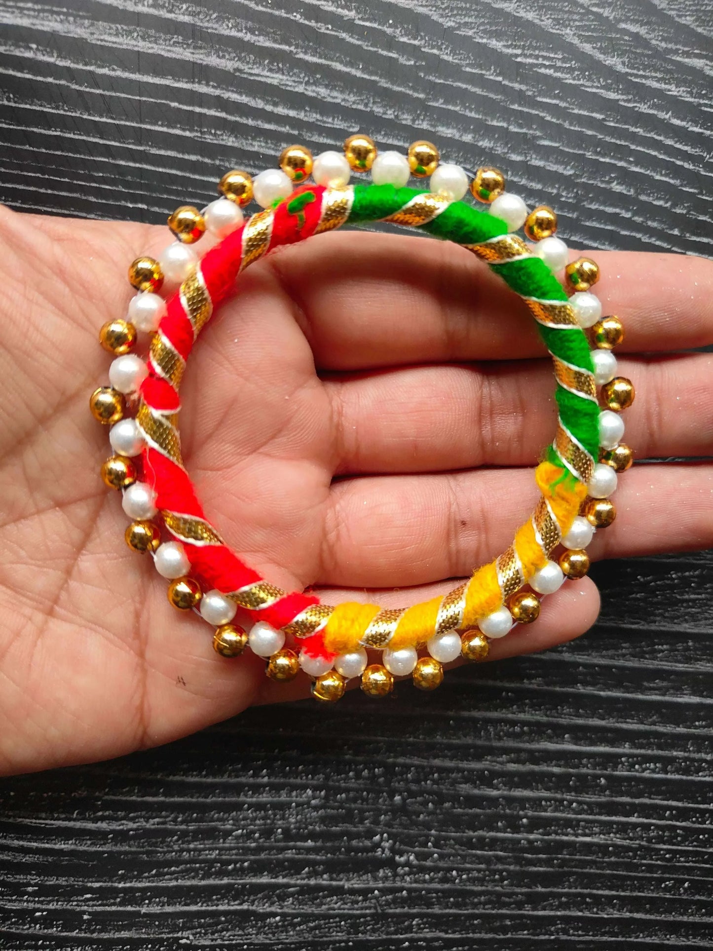 Multi-gota round ring on hand, striped red green yellow braids, pearl & gold beads