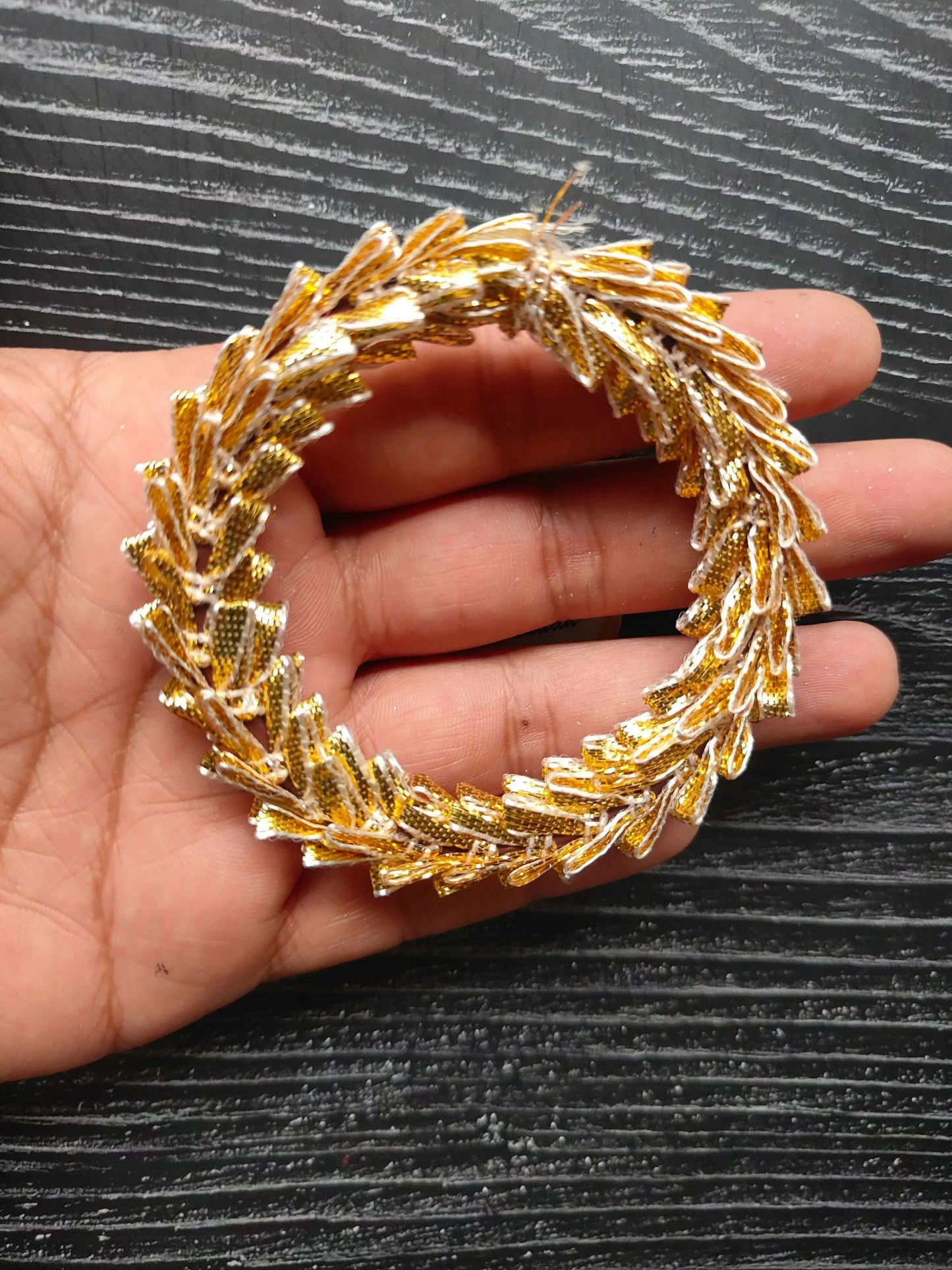Golden gota lace circular ring held in hand, intricate fringed braid texture