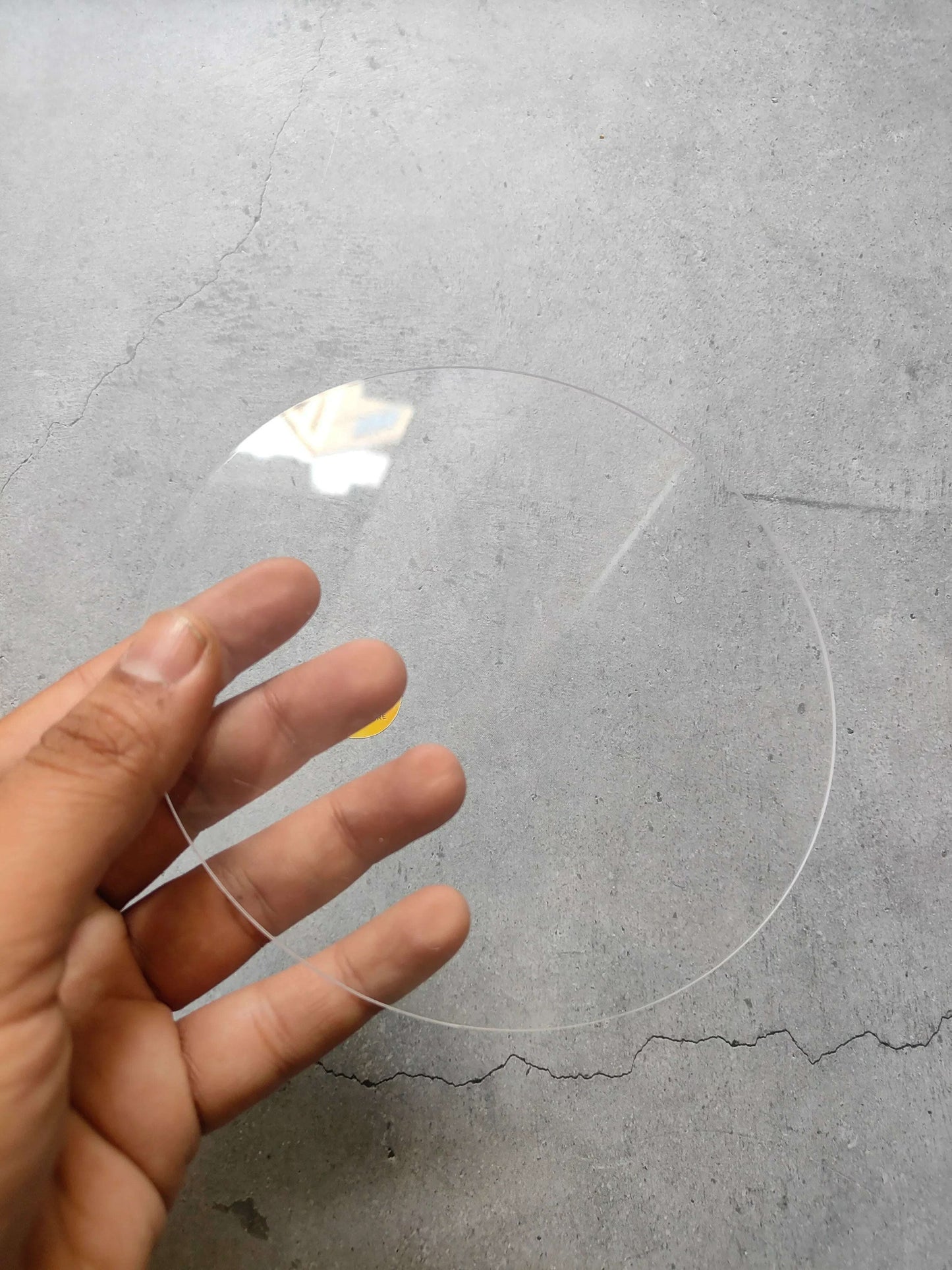 Clear round acrylic sheet held in hand, transparent circular disc