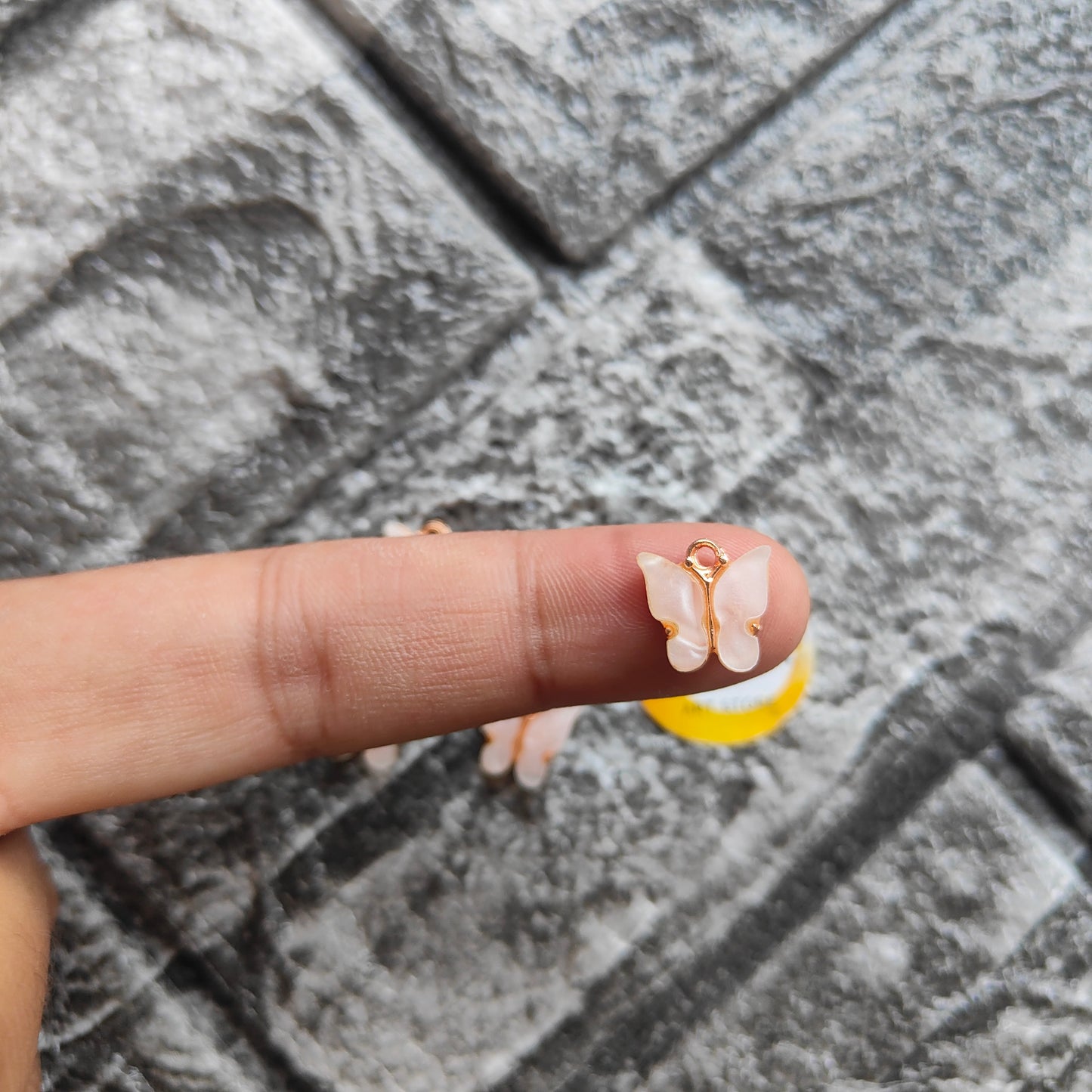 Delicate butterfly resin pendant charms displayed on a finger for jewelry making enthusiasts