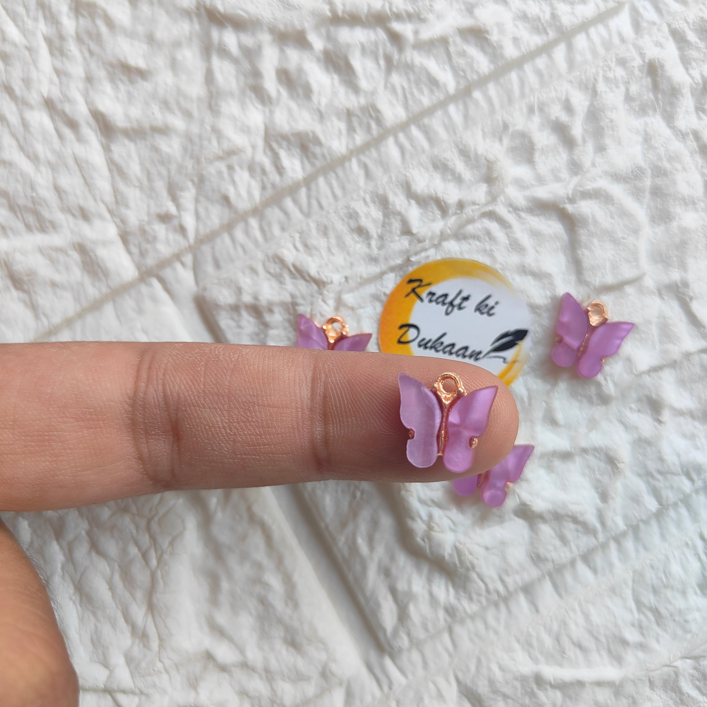 Hand holding purple butterfly resin pendant charms with gold accents for crafting and jewelry making