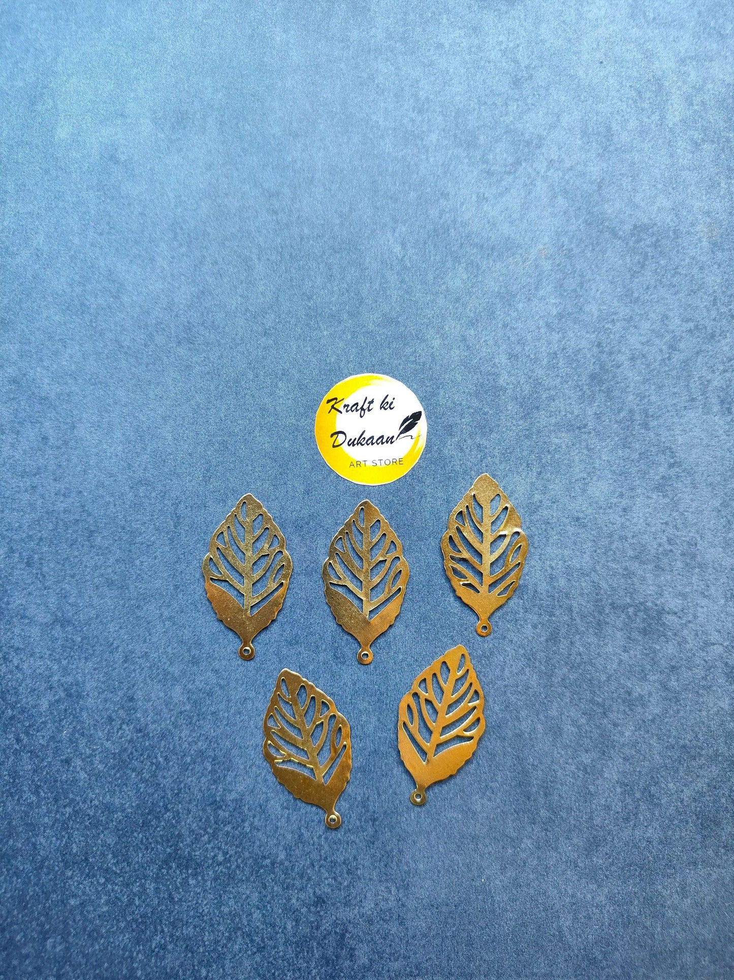Gold metal leaf embellishments, decorative leaf charms on a blue surface