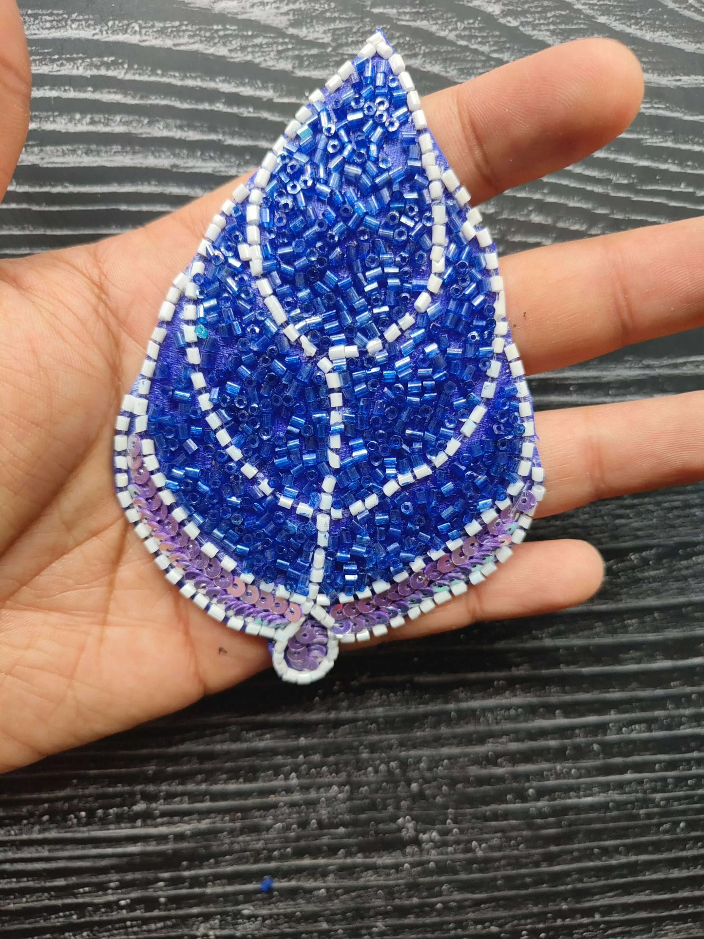 Blue teardrop decorative patch with white stitched lines and purple beaded border