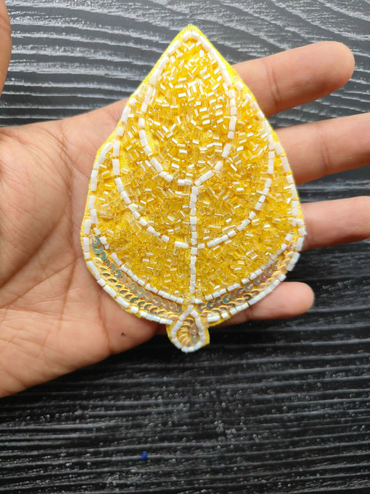 Yellow teardrop decorative patch with white stitched lines and beaded details