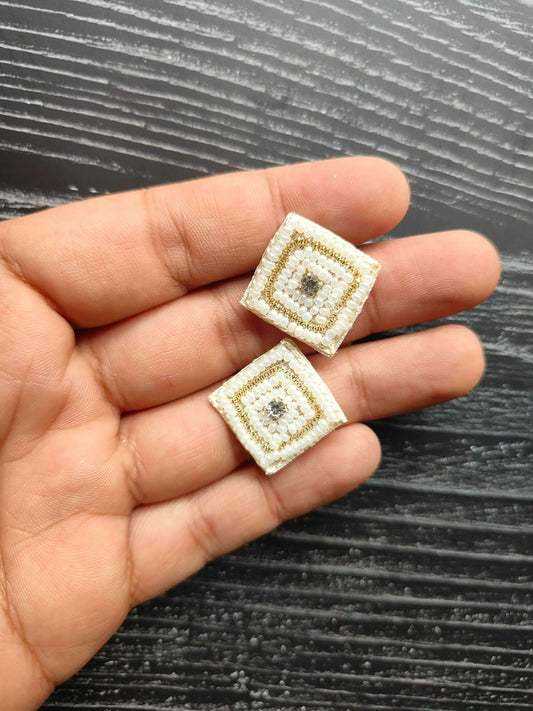 Small square beaded decorative patches on hand; ivory fabric, gold border, sparkly center