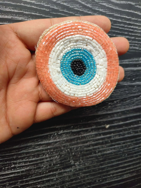 Light pink circular beaded eye patch with blue ring and black center