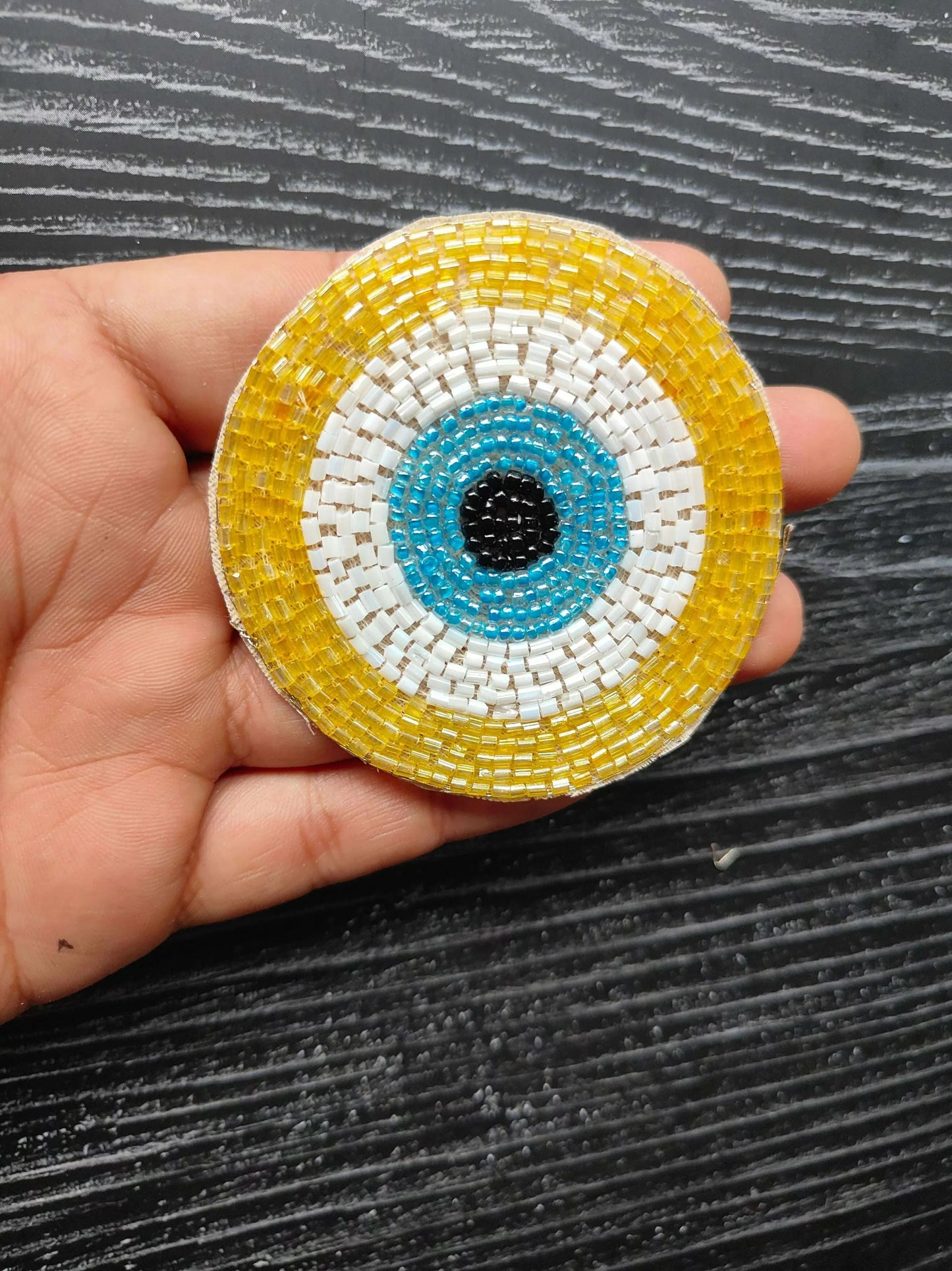 Yellow circular beaded eye patch with blue ring and black center, white border