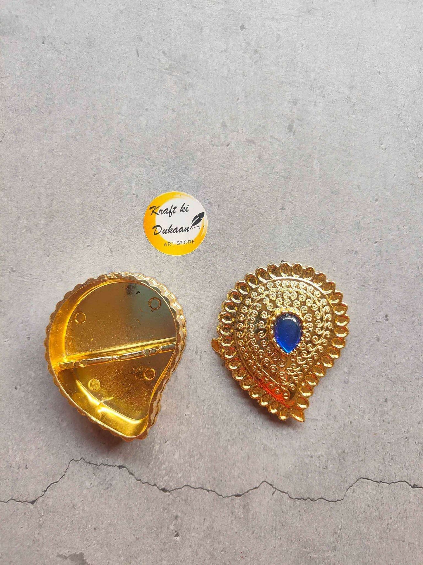 Gold-toned peacock motif with blue gemstone center; reverse side shown