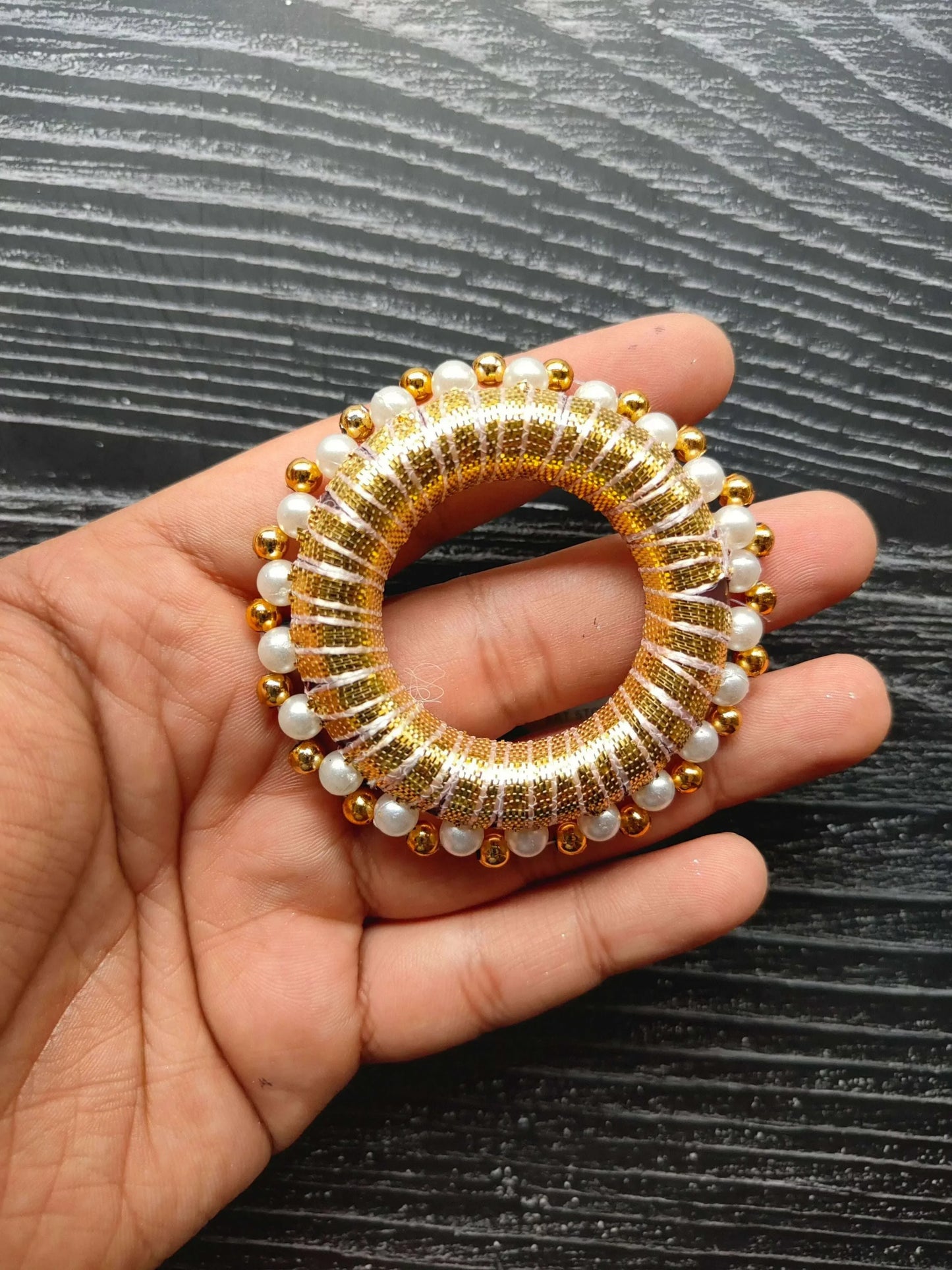 Close-up 2" round golden gota ring with pearl & gold beads, held in hand
