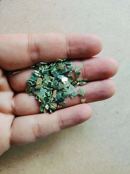 Hand holding shimmering green crystal chips for resin art showcasing small, reflective pieces