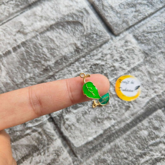 Green leaf metal charm with gold-tone loop on a fingertip, enamel leaf detail
