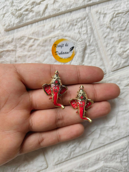 Two red Ganpati Ganesha enamel charms with gold accents on palm