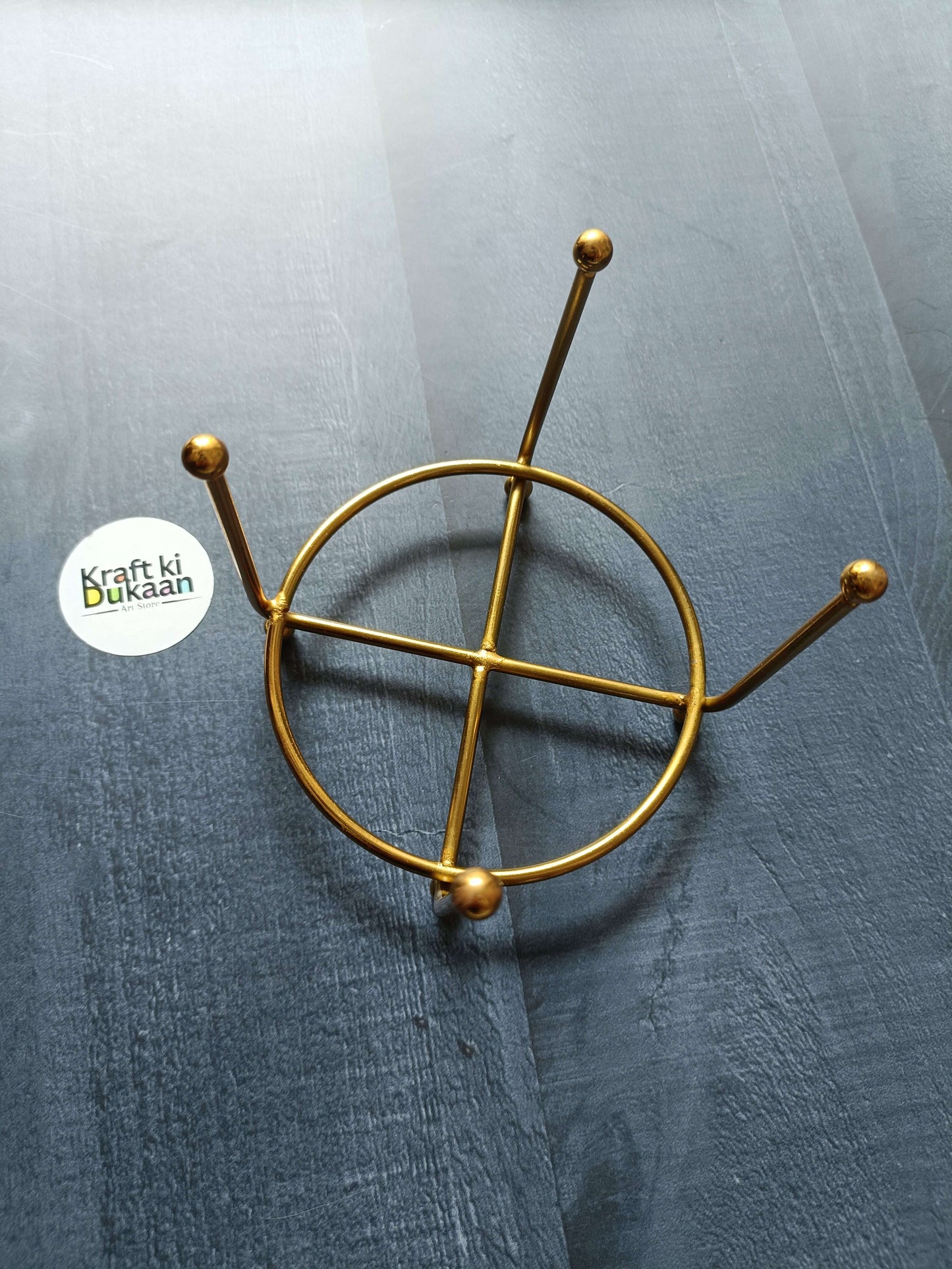 Gold metal coaster stand with circular ring and angled vertical arms with ball ends