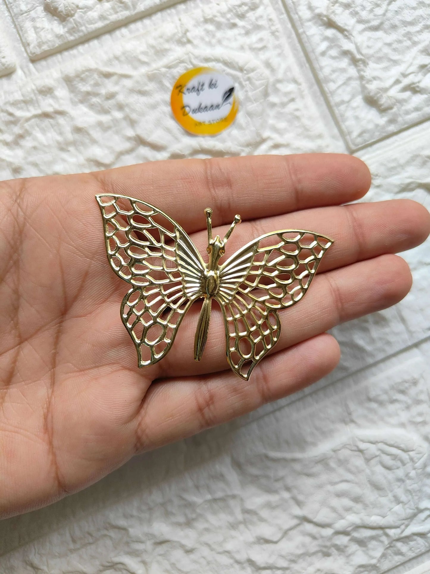 Gold-tone metal butterfly charm with filigree wings, held in hand with loop