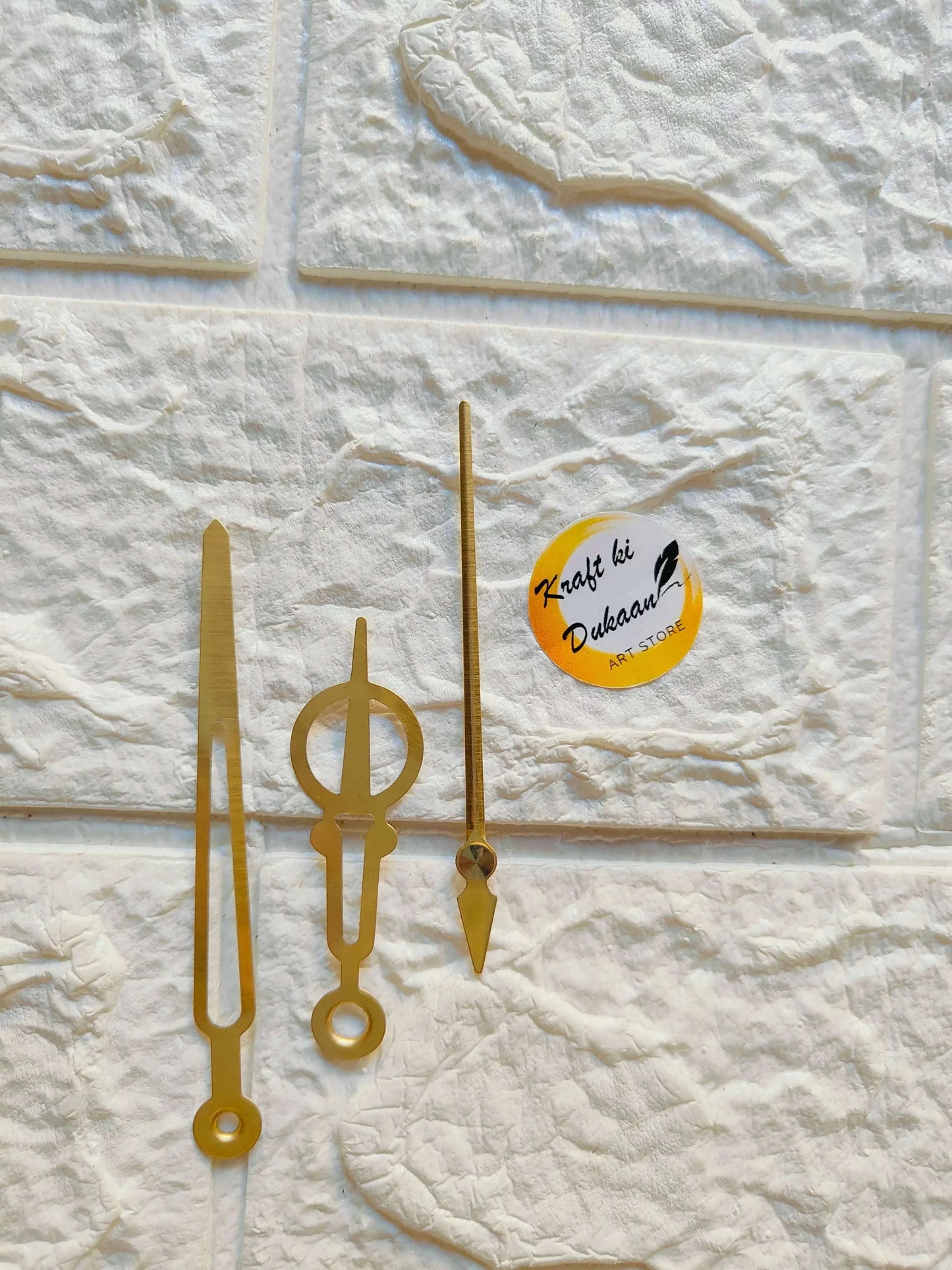 Metal clock hands set in gold, three hands with circular bases on display.