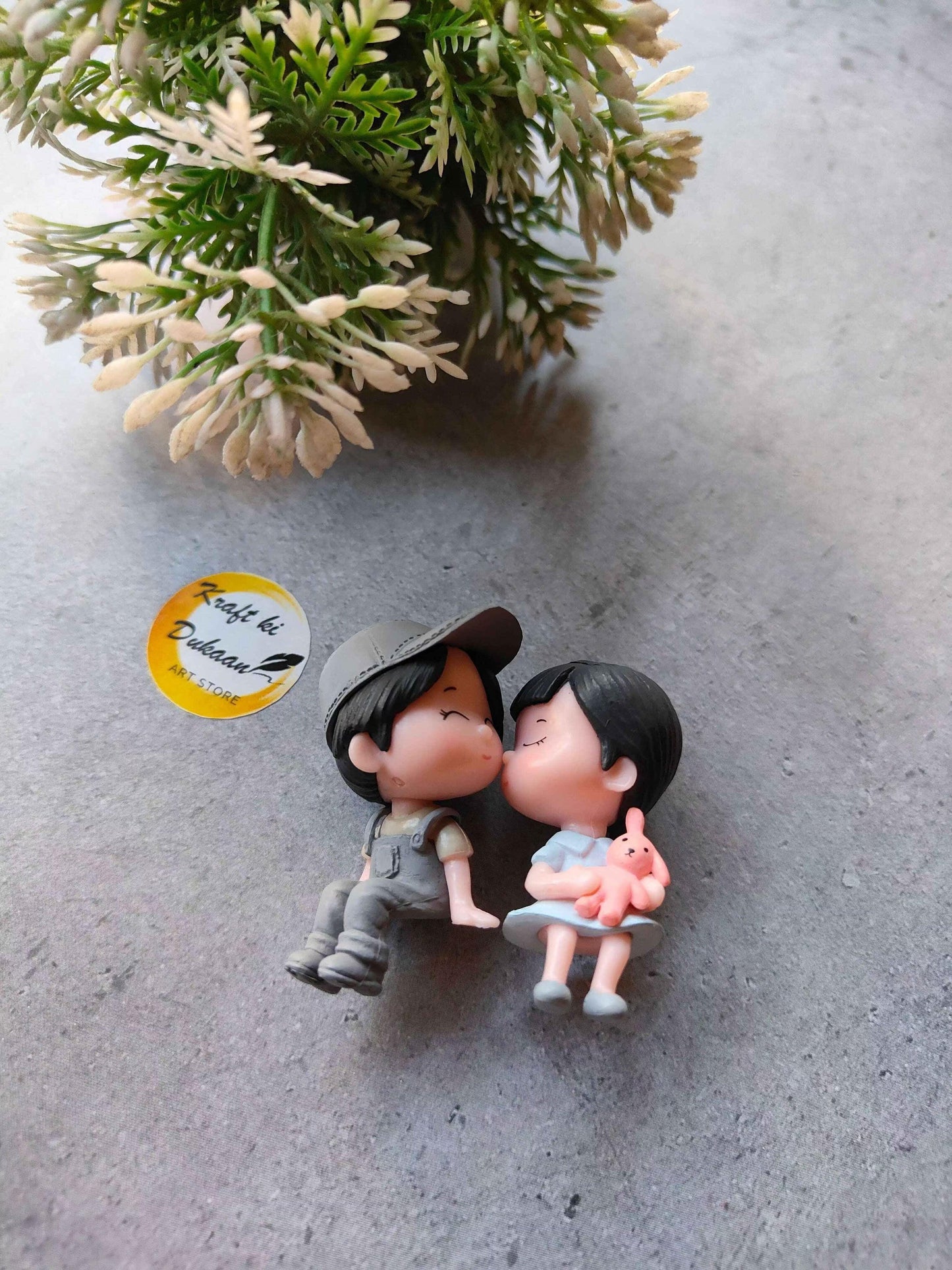 Miniature Model A2: two cartoon figures kissing; dark cap, one holds a pink pig toy
