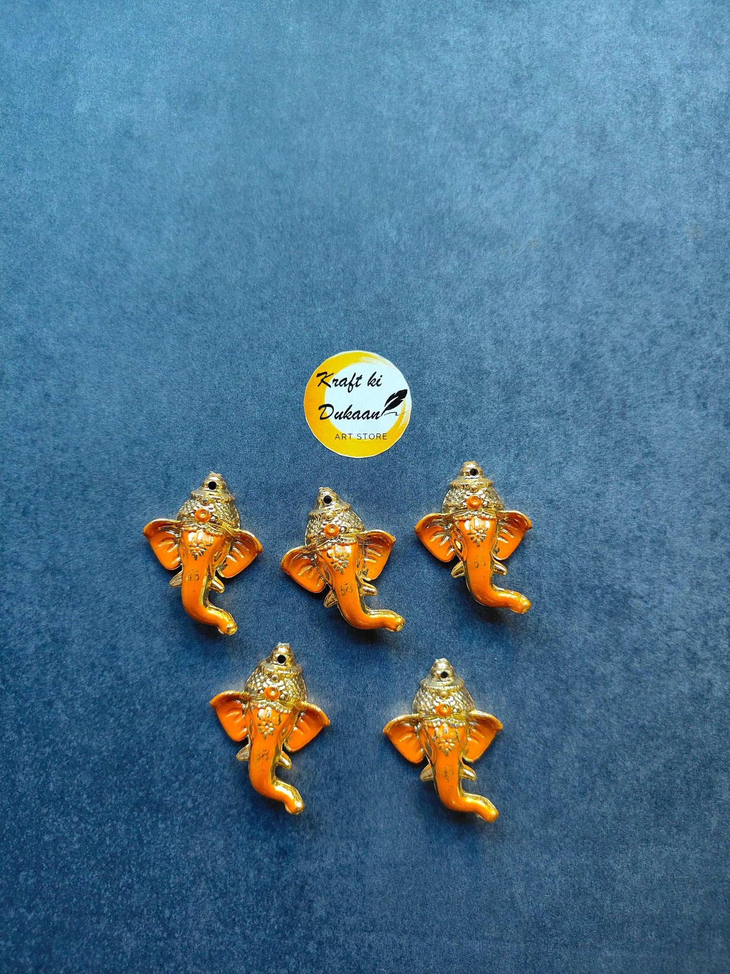 Orange Ganpati face pack—small Ganesh face pins, 5 shown on a blue background