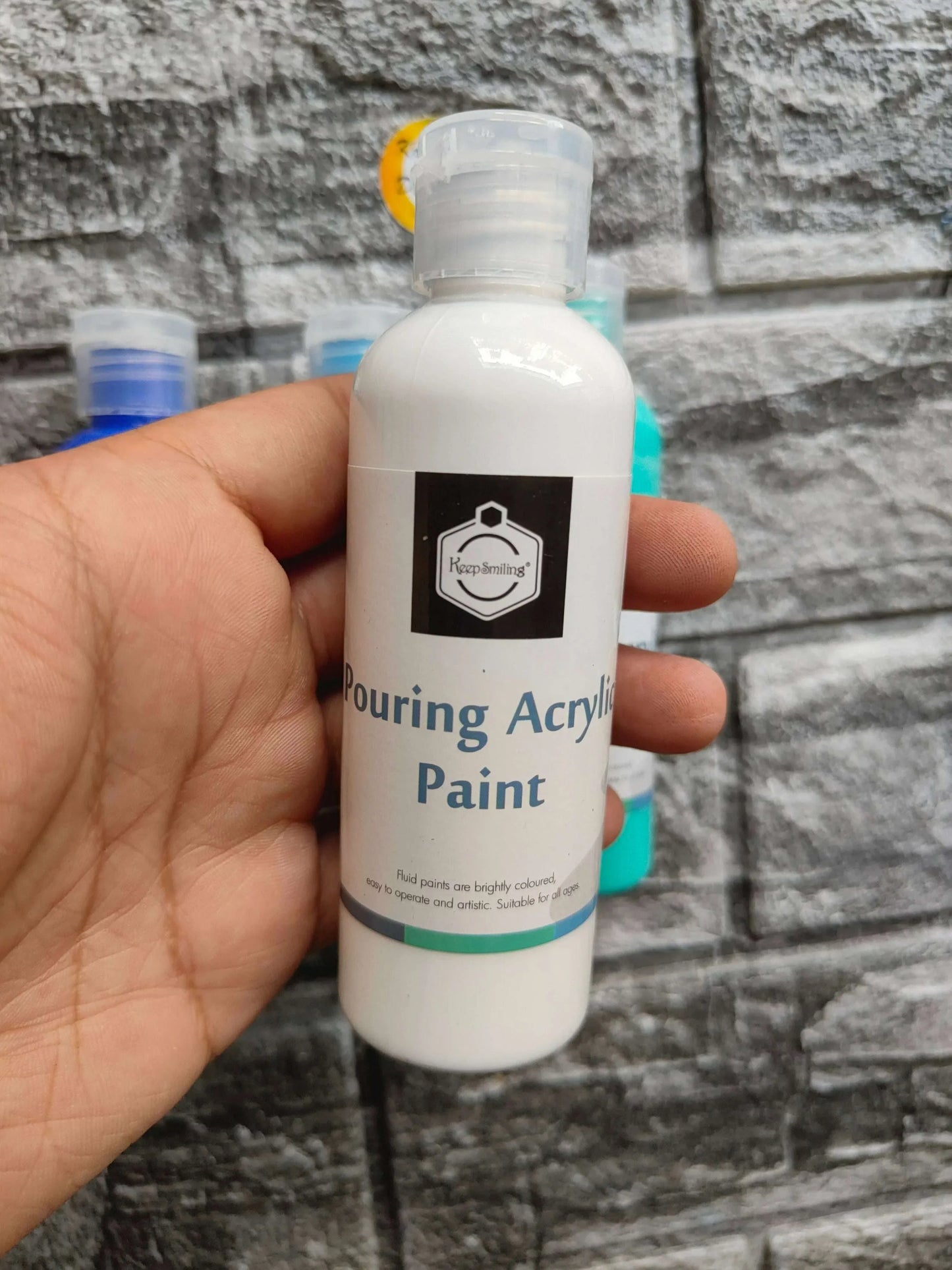 Hand holding white pouring acrylic paint bottle.