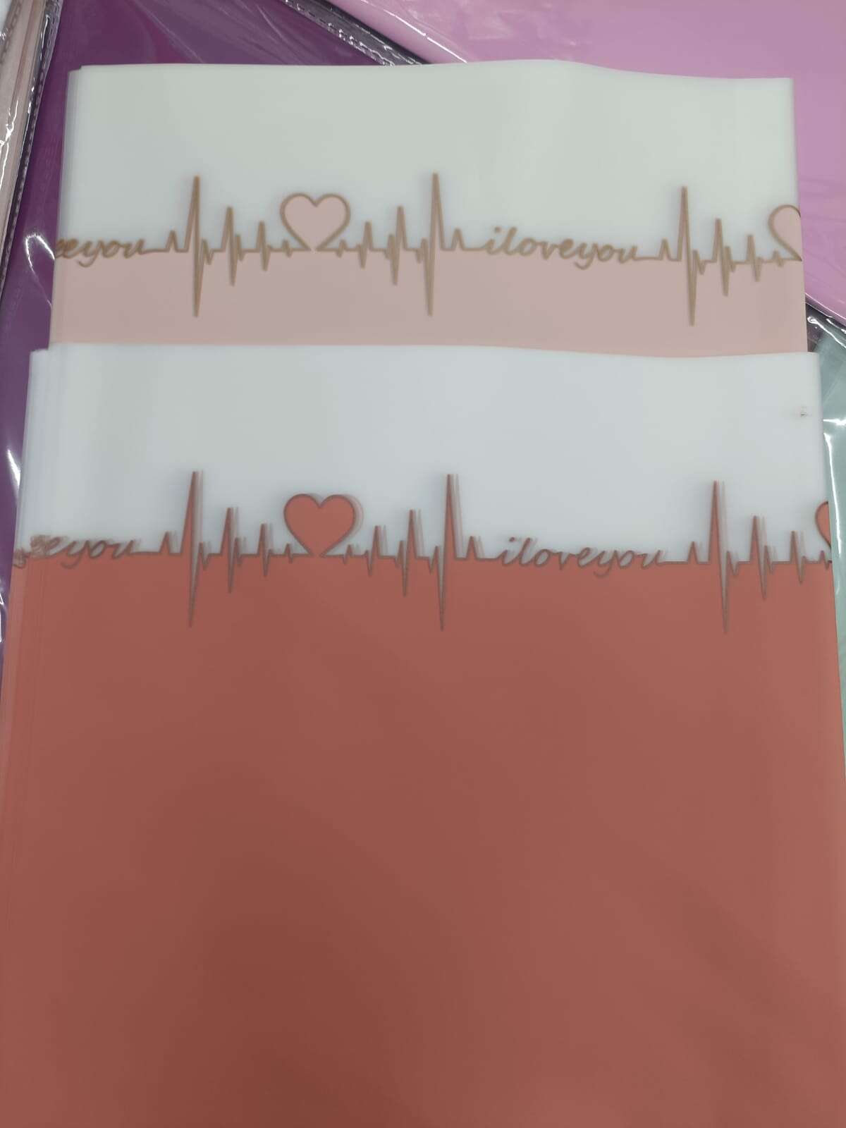 Two wrapping paper sheets, blue and orange, with gold ECG line and heart pattern