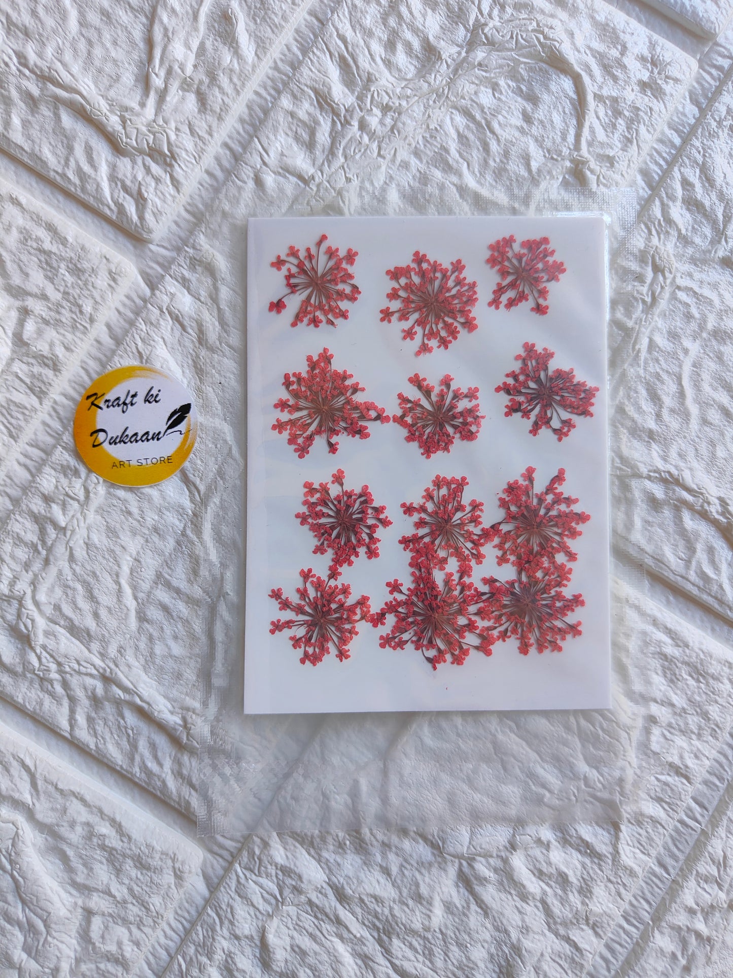 Pressed flower art supplies featuring vibrant red floral designs on a white sheet