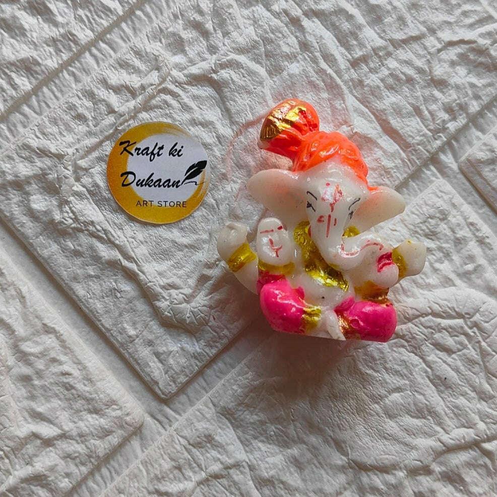Ganpati idol front view, orange crown, white skin, pink lower wear, golden highlights