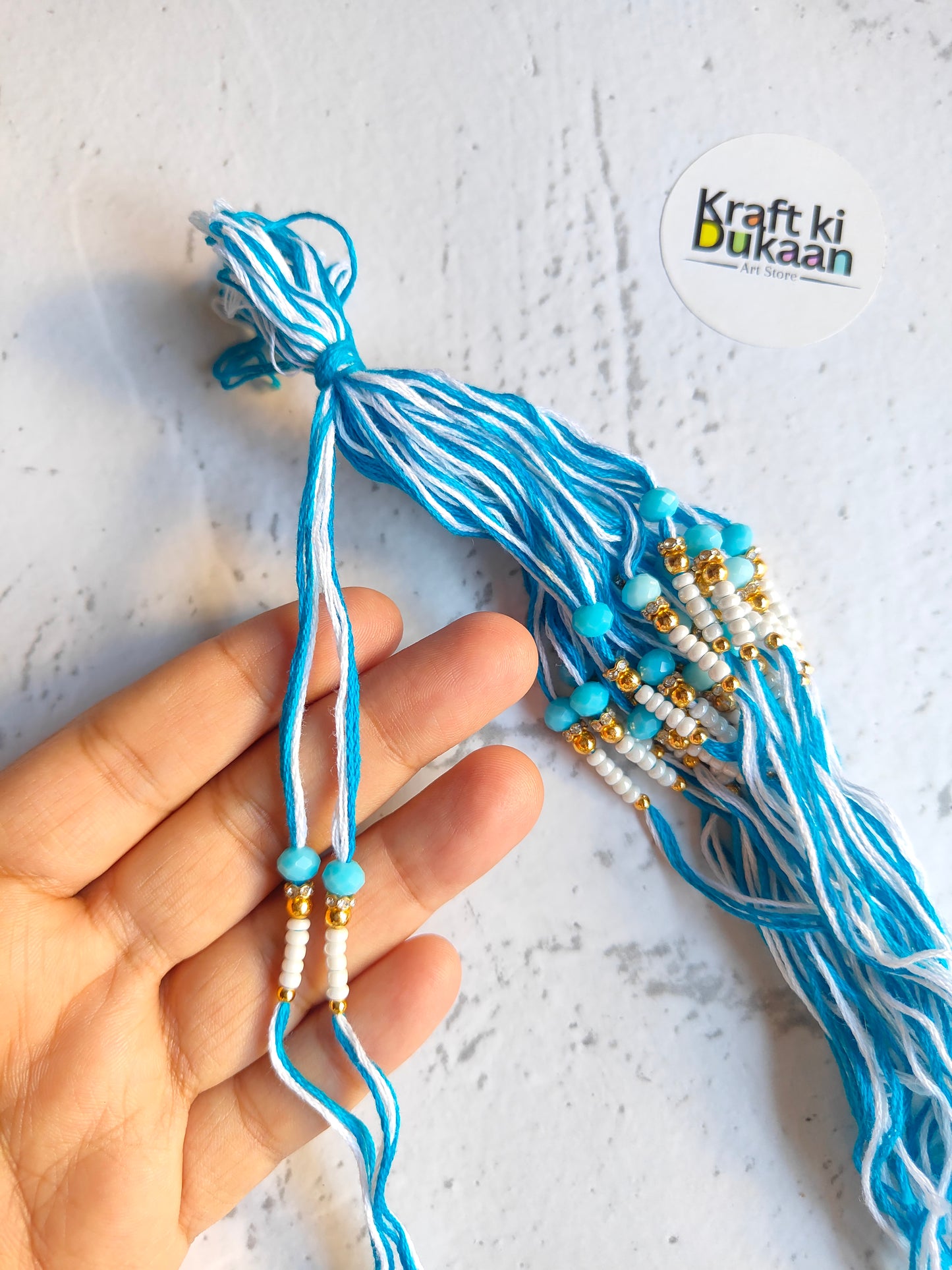 Blue rakhi thread with bead drops and knotted ends, held in hand