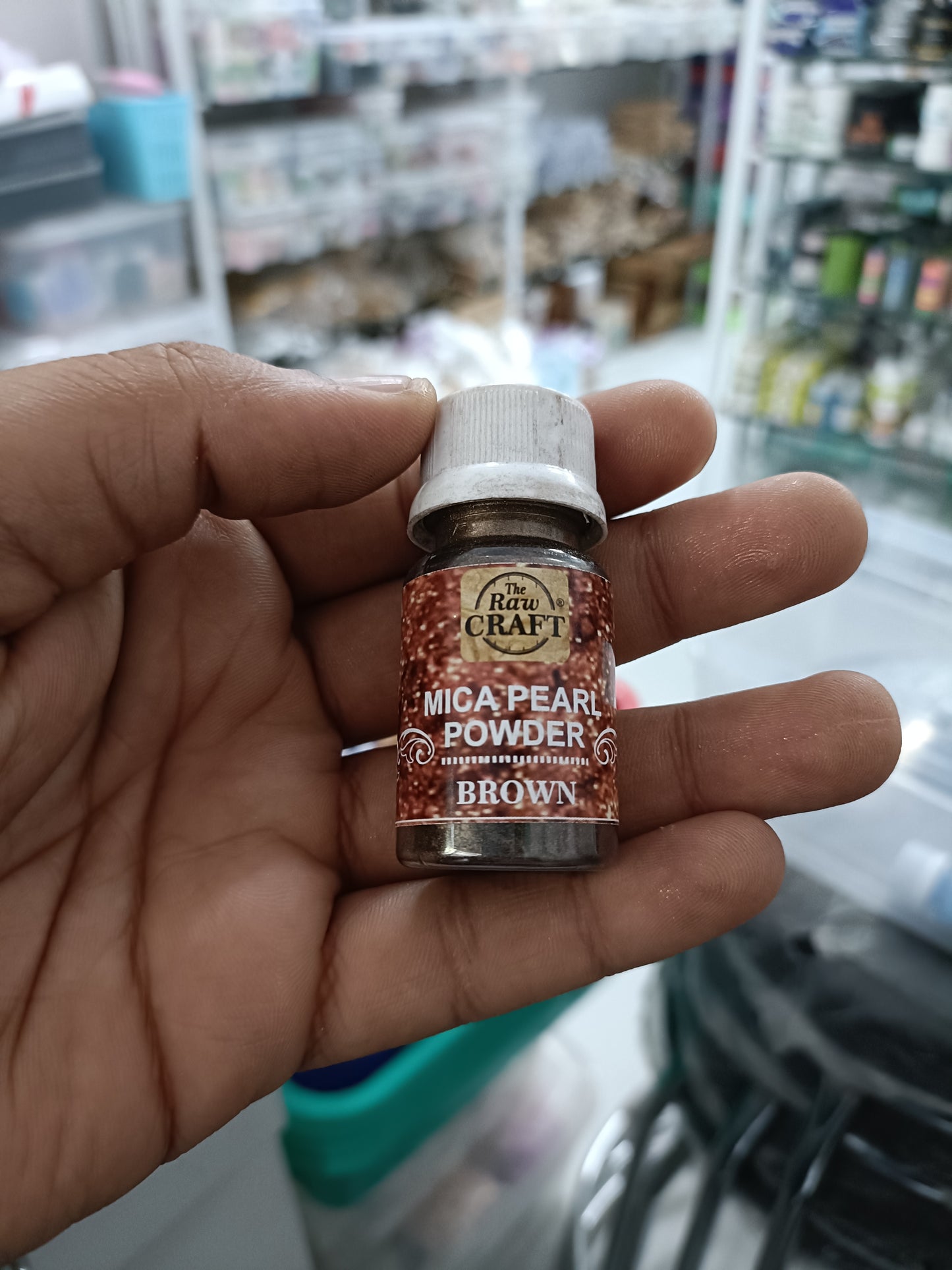 MICA pearl powder bottle, brown colorant, held in hand with screw cap.
