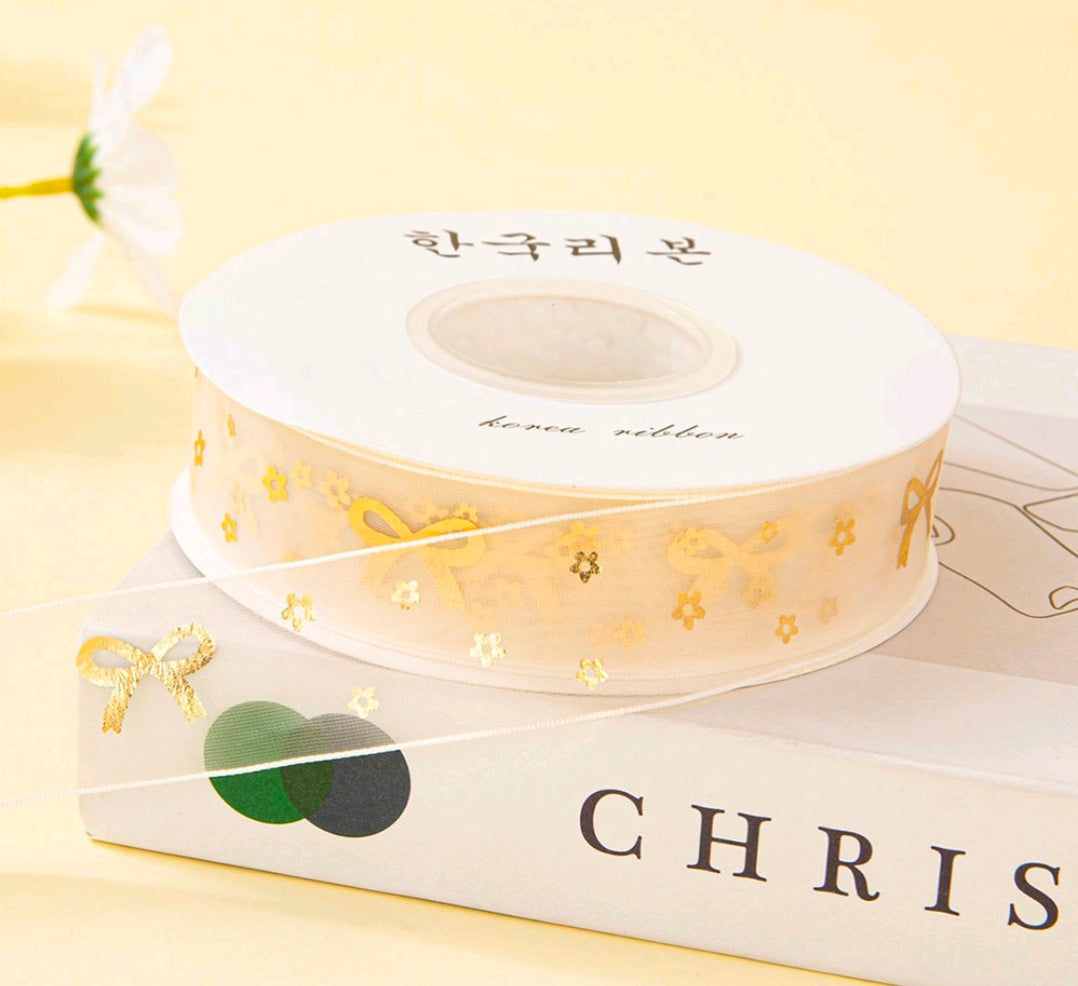 White ribbon spool with sheer gold floral print, decorative craft ribbon roll