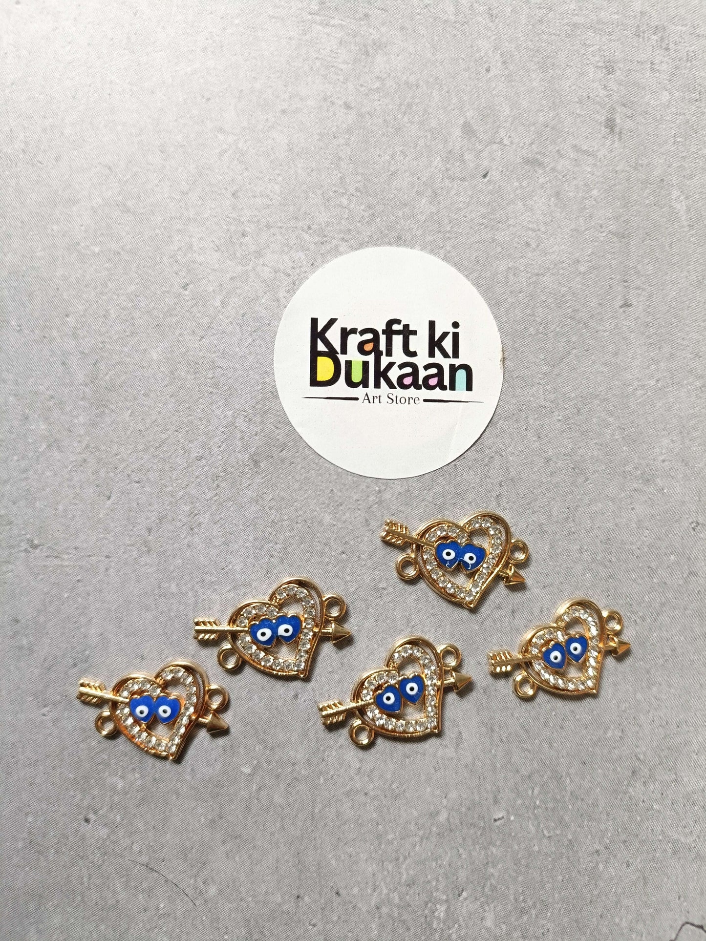 Five gold-tone heart evil-eye bracelet charms with blue centers, small hanging loops