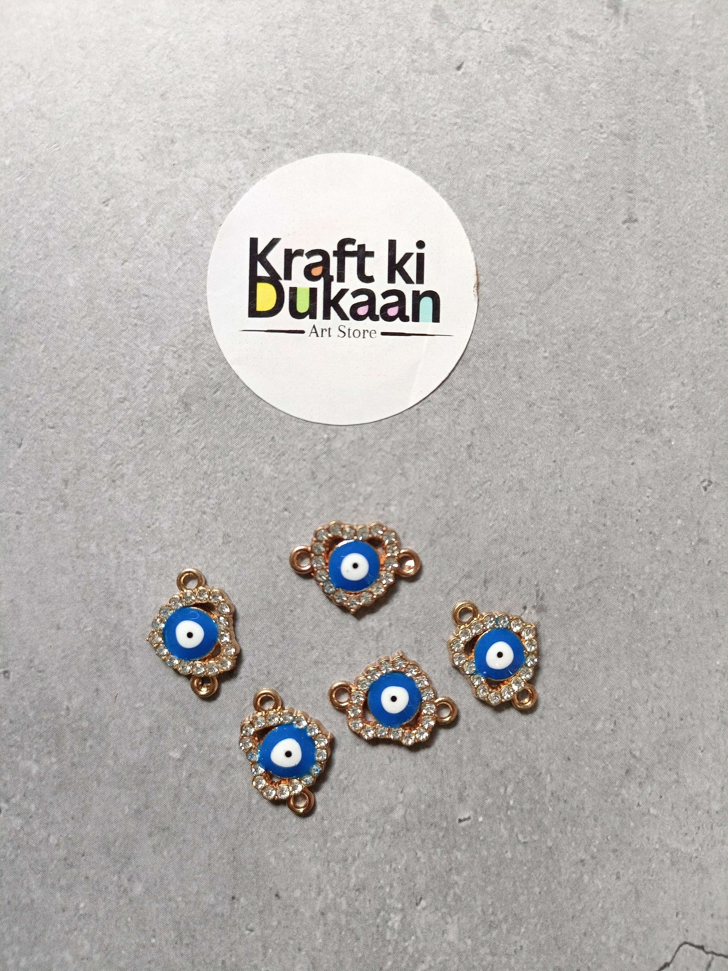 Five evil eye bracelet charms, blue center with gold-tone edging, arranged on surface