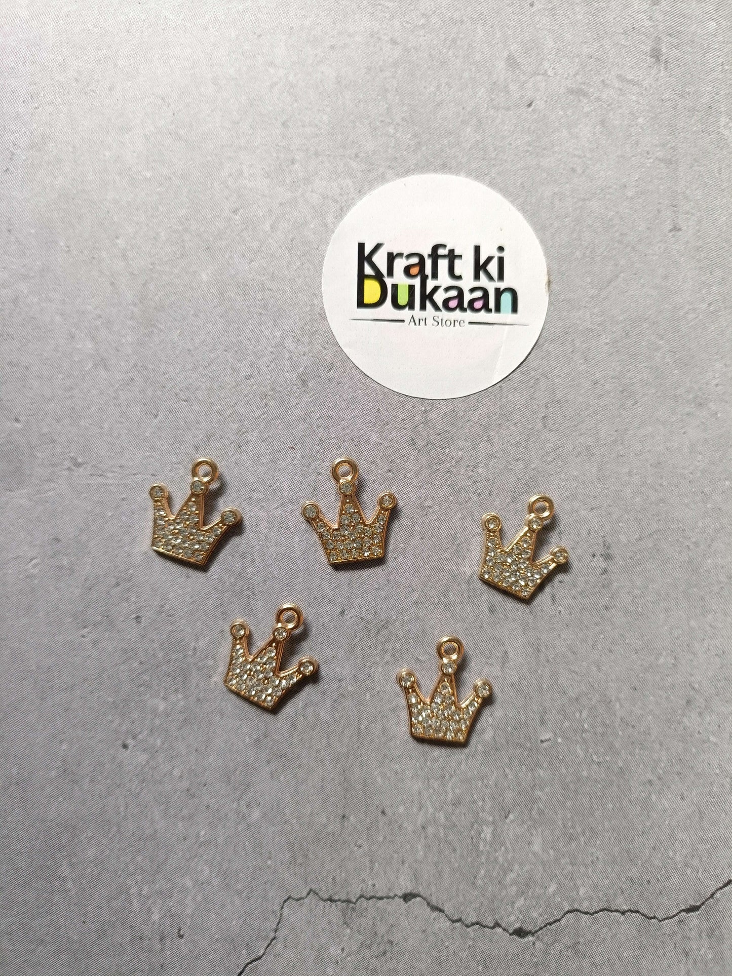 Gold crown pendant charms with rhinestone sparkle, five-piece set laid on surface