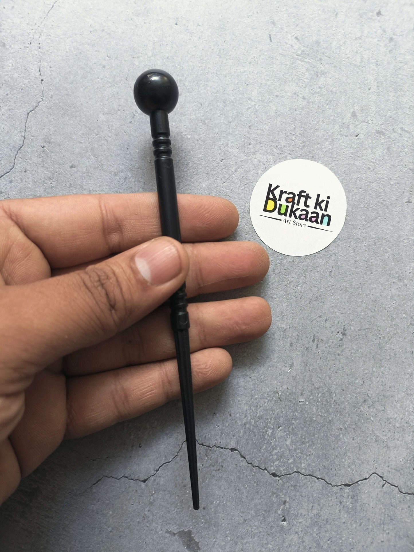 Black clay modelling ball-end tool with slim rod, held in hand