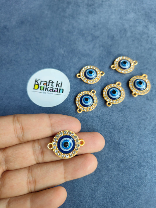 Gold-toned evil eye rakhi pendant with blue center, held in hand; set of 6