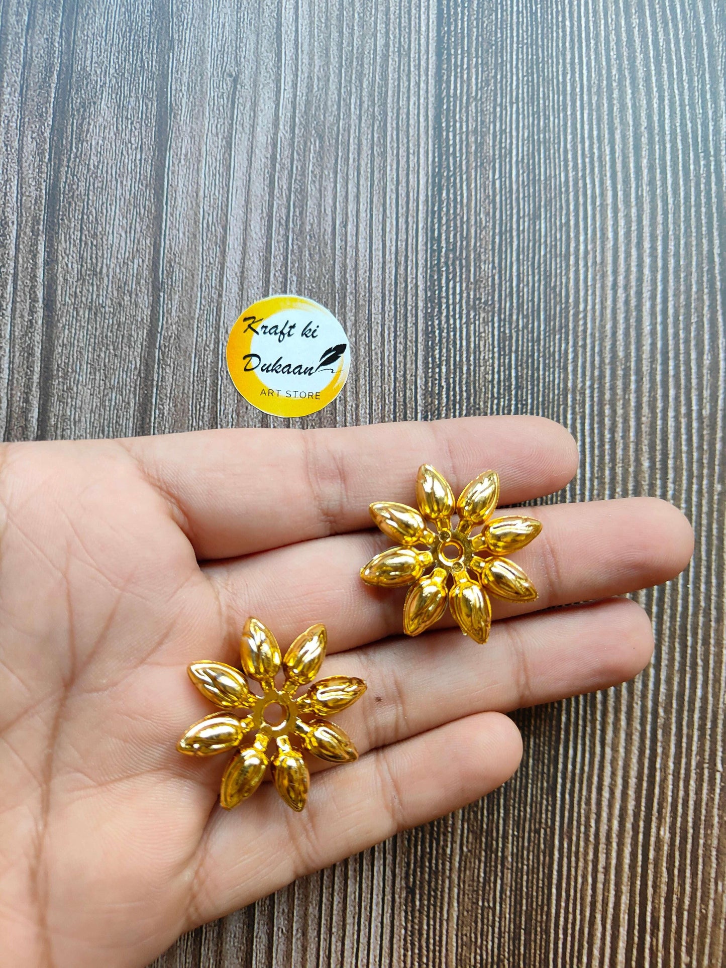 Golden flower design beads, two gold-toned floral beads held between fingers