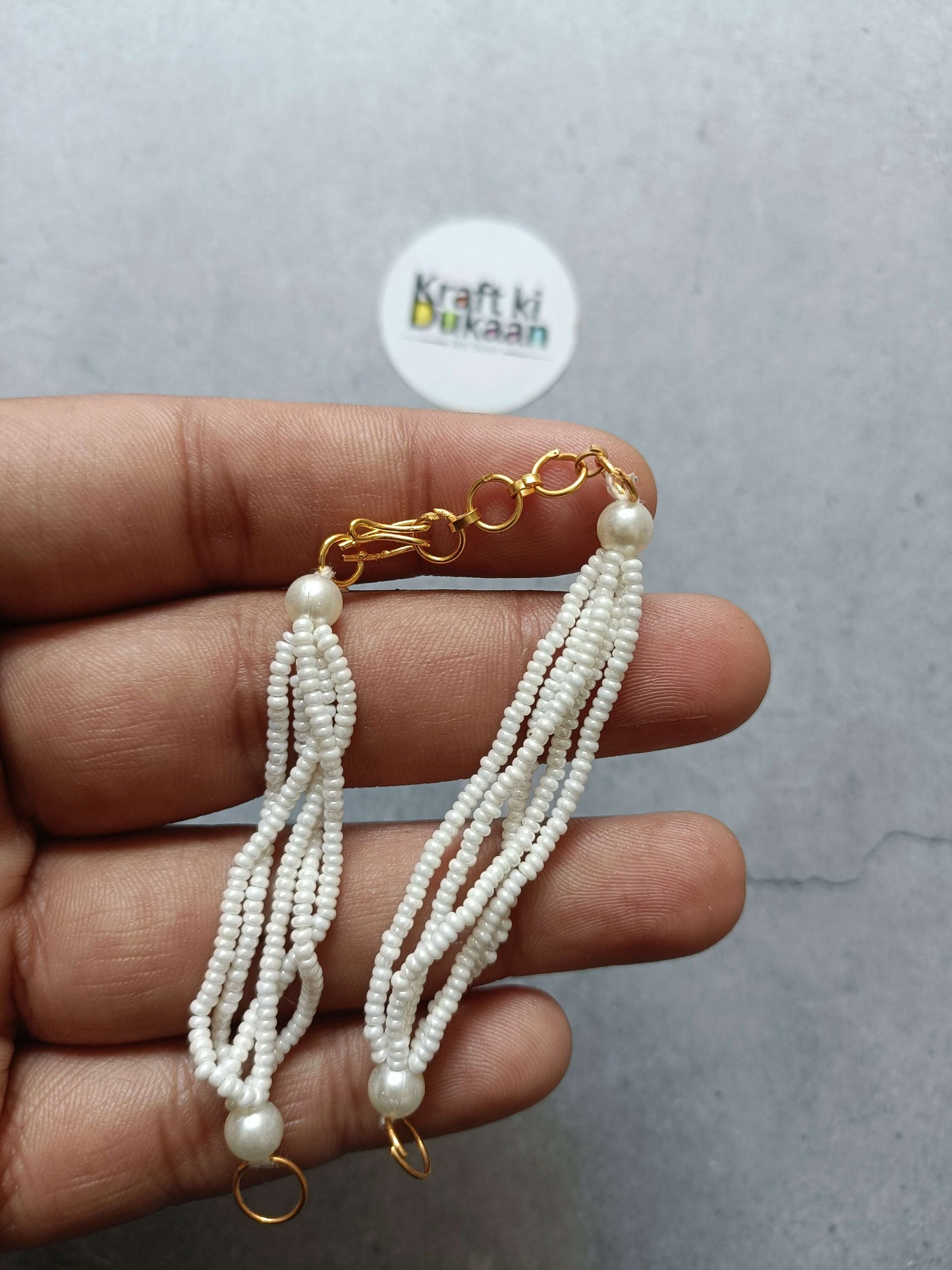 Gold link beaded bracelet with white pearl tassel strands and clasp ring, close-up