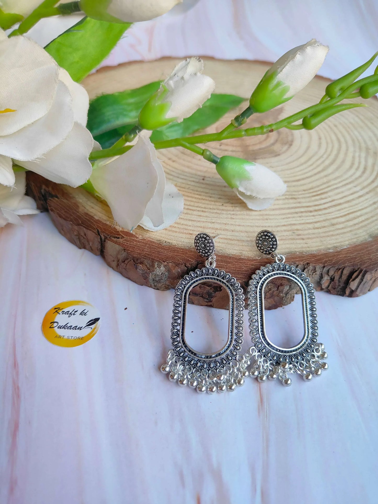 Silver oval jhumka earrings with detailed filigree and dangling bell-style drops