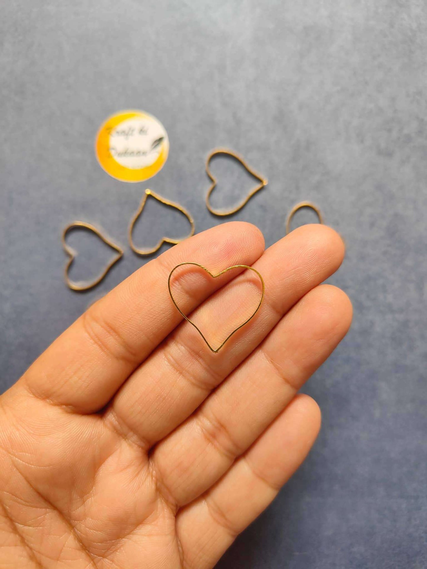 Heart bezel earring findings set—gold-tone outline heart in hand view