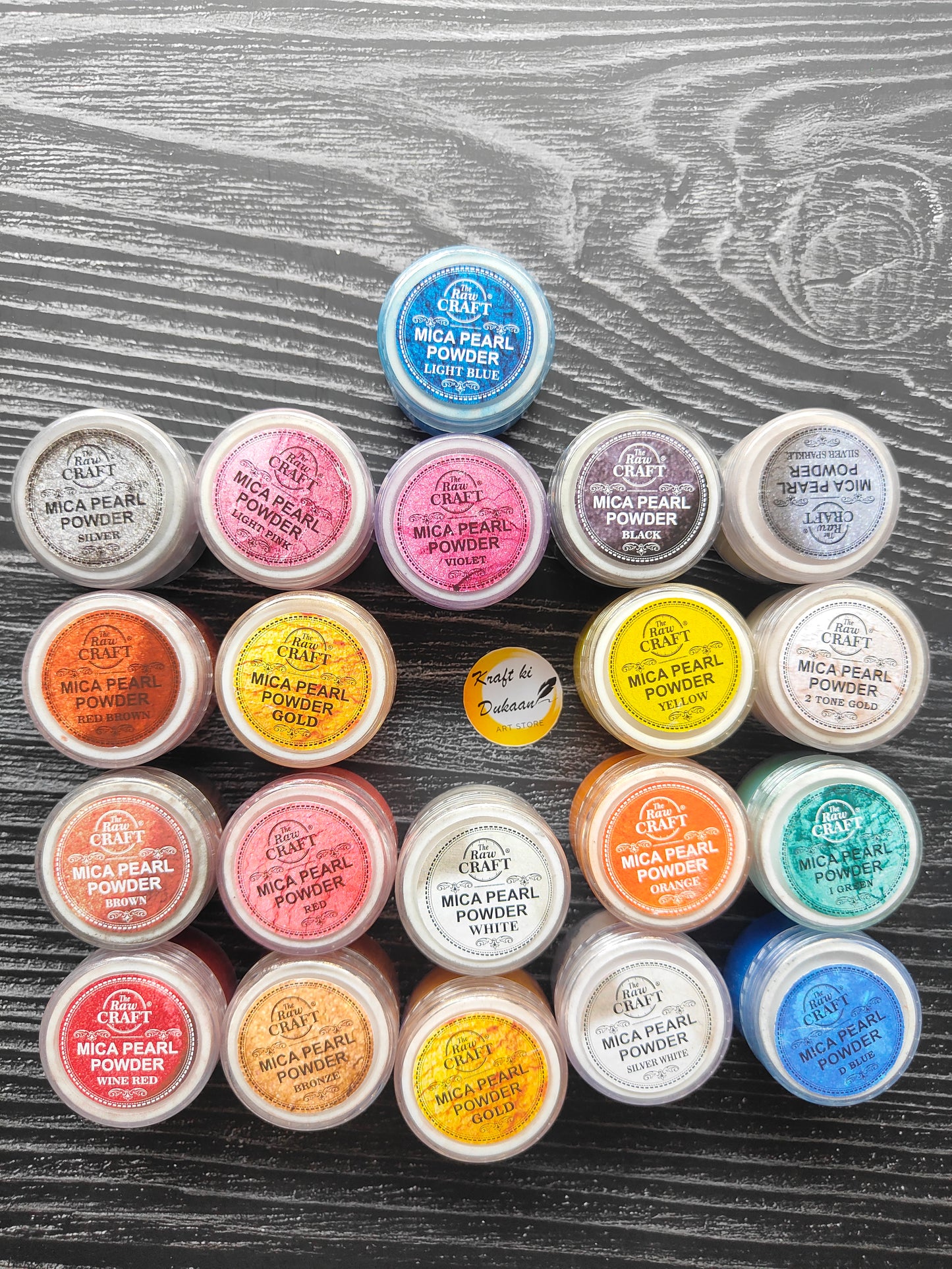 Variety of vibrant MICA pearl powder for resin in different colors in plastic containers arranged on a wooden background