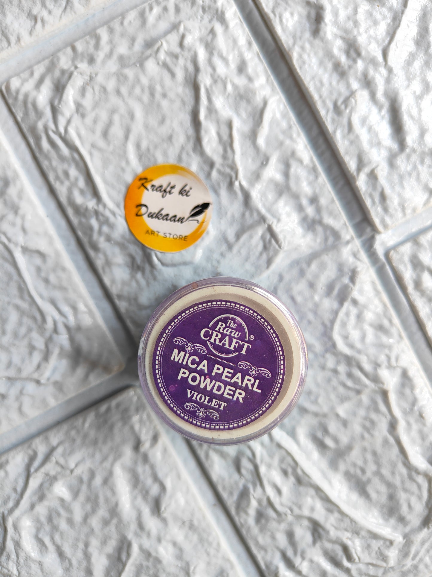 Kraft ki Dukaan MICA pearl powder for resin in Violet color shown with a branded button on textured surface