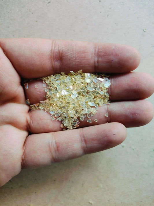 A hand holding a handful of yellow resin crystals showcasing their translucent glittering texture