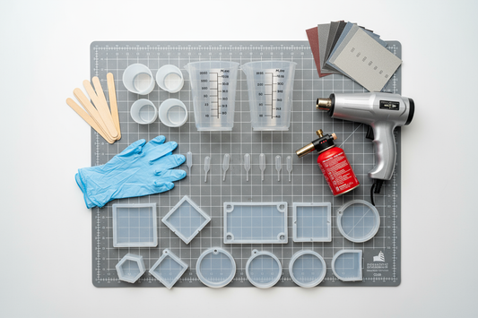 Beginner resin art tools including molds, measuring cups, and a heat gun on a crafting mat