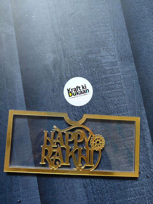 Golden acrylic Rakhi envelope with “HAPPY RAKHI” text and gear-style motif
