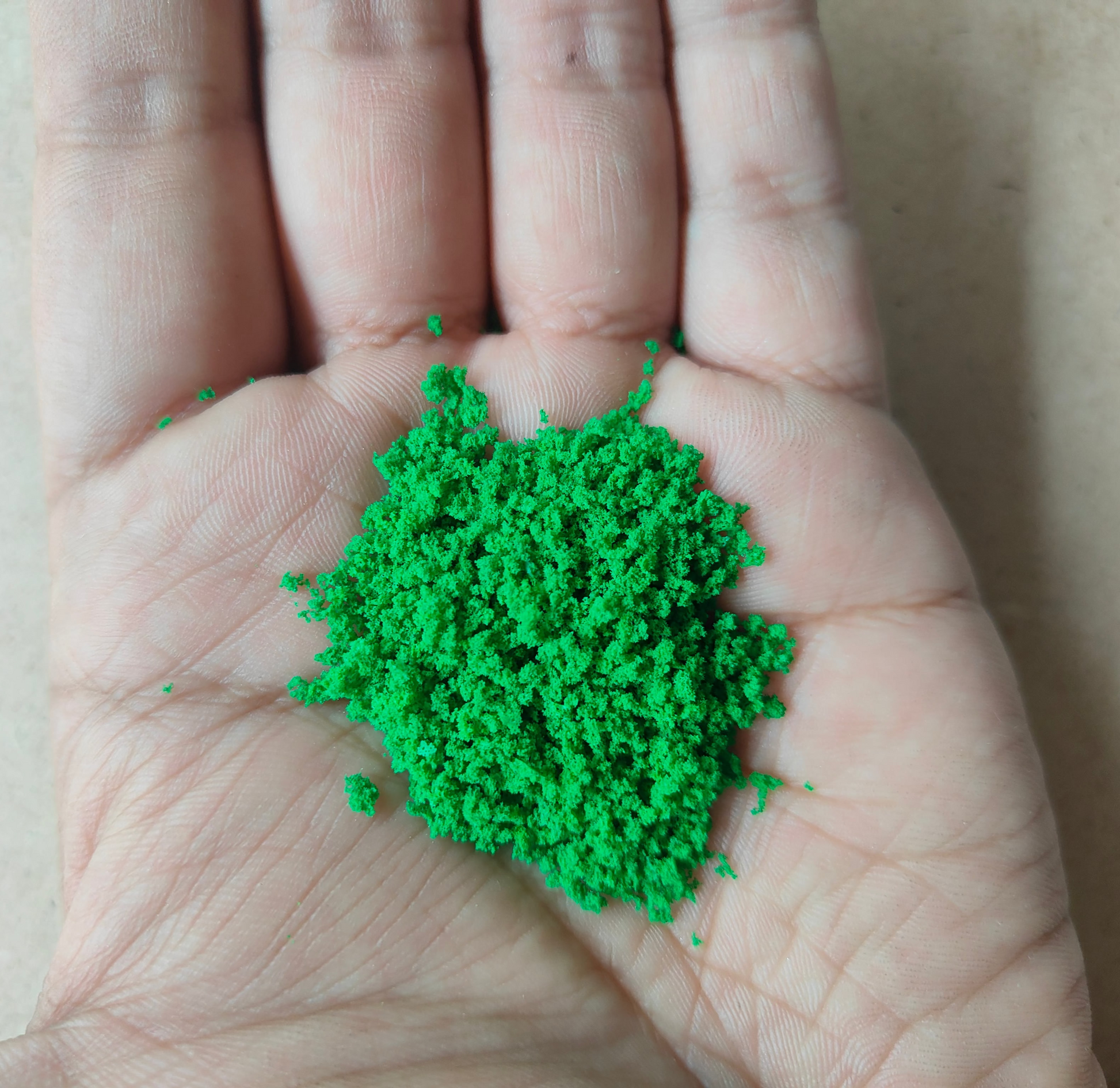 Hand holding vibrant green artificial moss for resin art, ideal for crafting and decoration