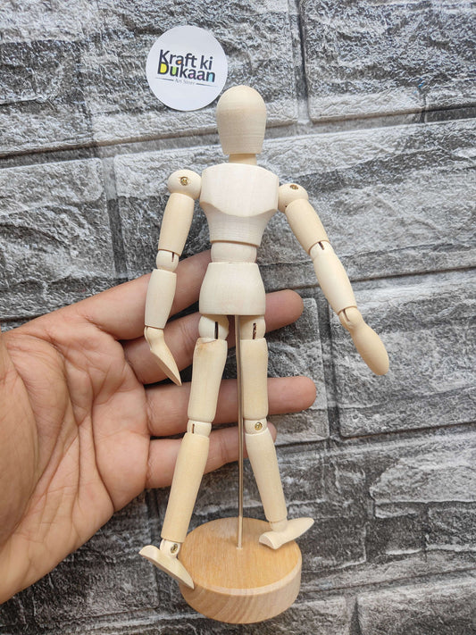 Wooden manikin close-up: jointed torso and limbs on round base, held in hand