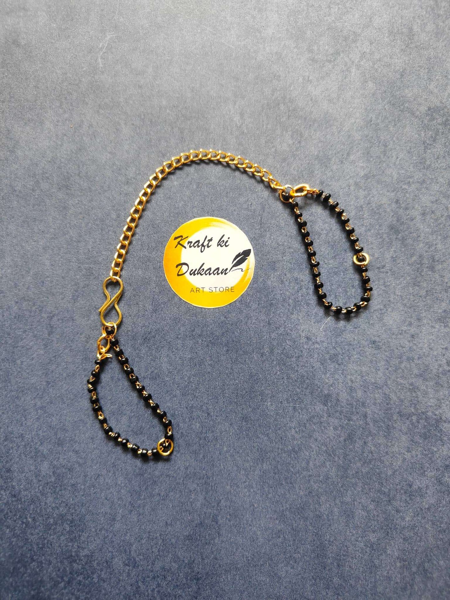 Rakhi bracelet chain with gold-tone top chain and black bead drape, small circular charm