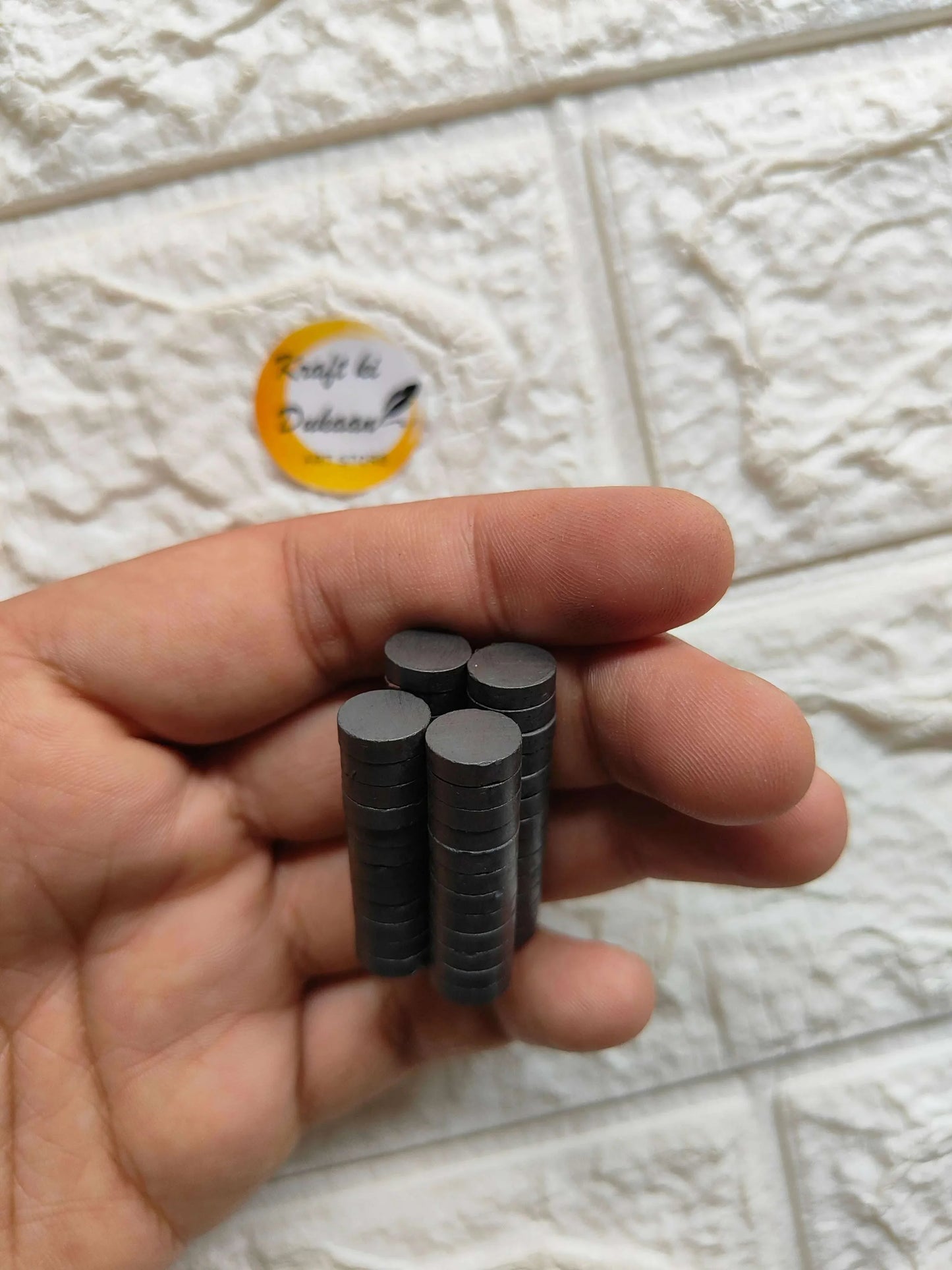 Hand holding black round magnets, 10x3mm size, 50-pack