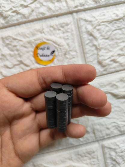 Hand holding black round magnets, 10x3mm size, 50-pack